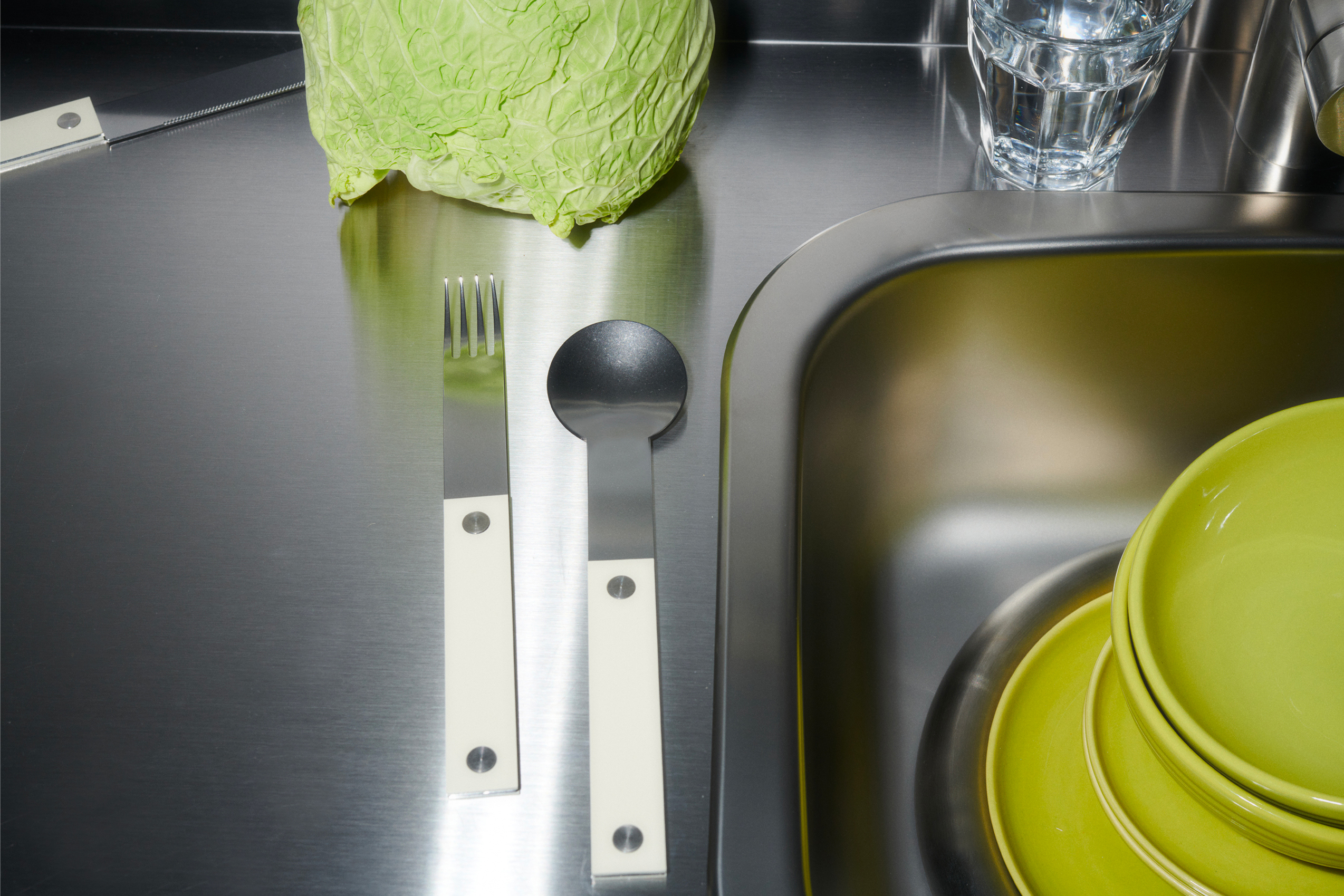 forks-plus-flatware-almond-handle-sink-lettuce-dishware Stainless steel flatware with almond-colored handles on stainless surface, green dishware and lettuce in corner of sink
