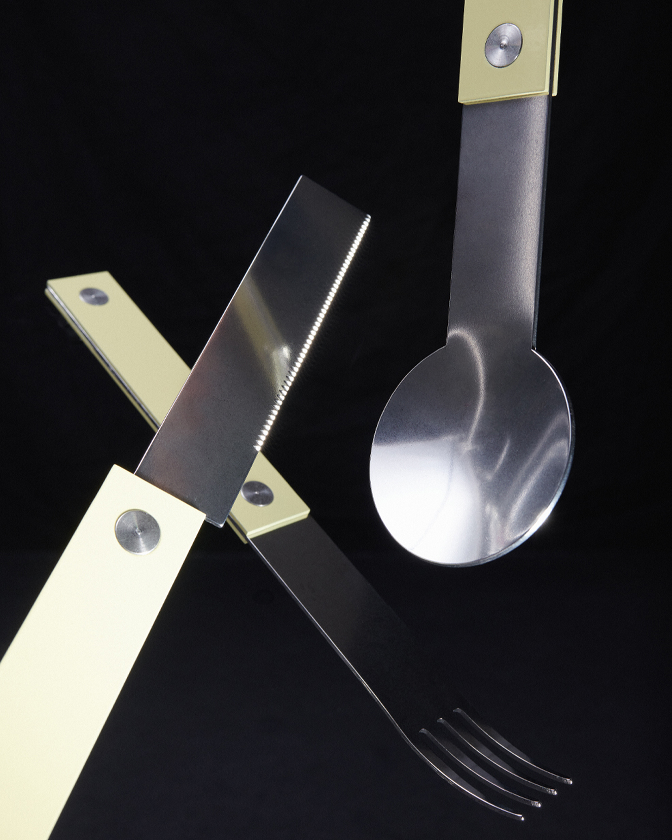 forks-plus-flatware-trio-butter-handles-black-background Trio of stainless steel fork, knife, and spoon with butter-colored riveted handles on black background