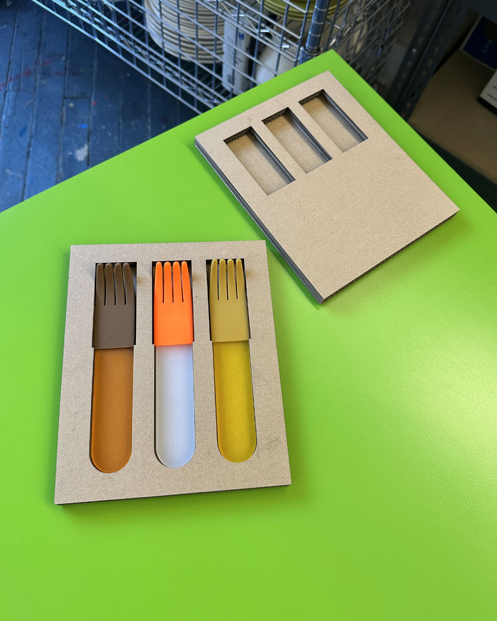 Trio of orange acrylic forks in cardboard packaging on green surface