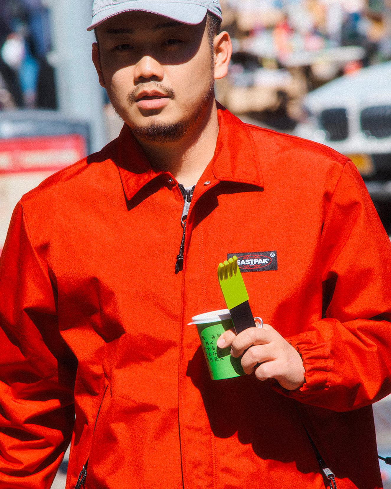 forks-plus-jinu-red-jacket-black-fork-green-sleeve-city Man in baseball hat and red jacket holding a green coffee cup and black fork with green silicone sleeve in city setting