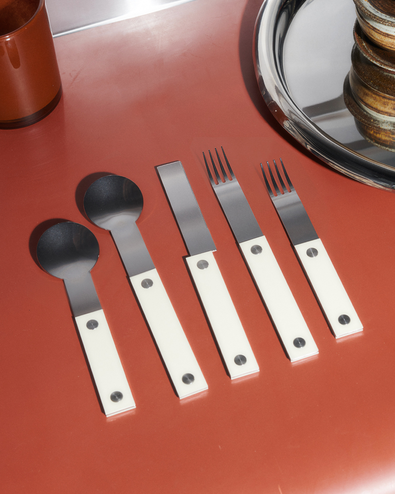 forks-plus-almond-flatware-amber-surface-steel-tray 5-piece almond-handled flatware set on amber-colored surface with stainless steel tray in corner