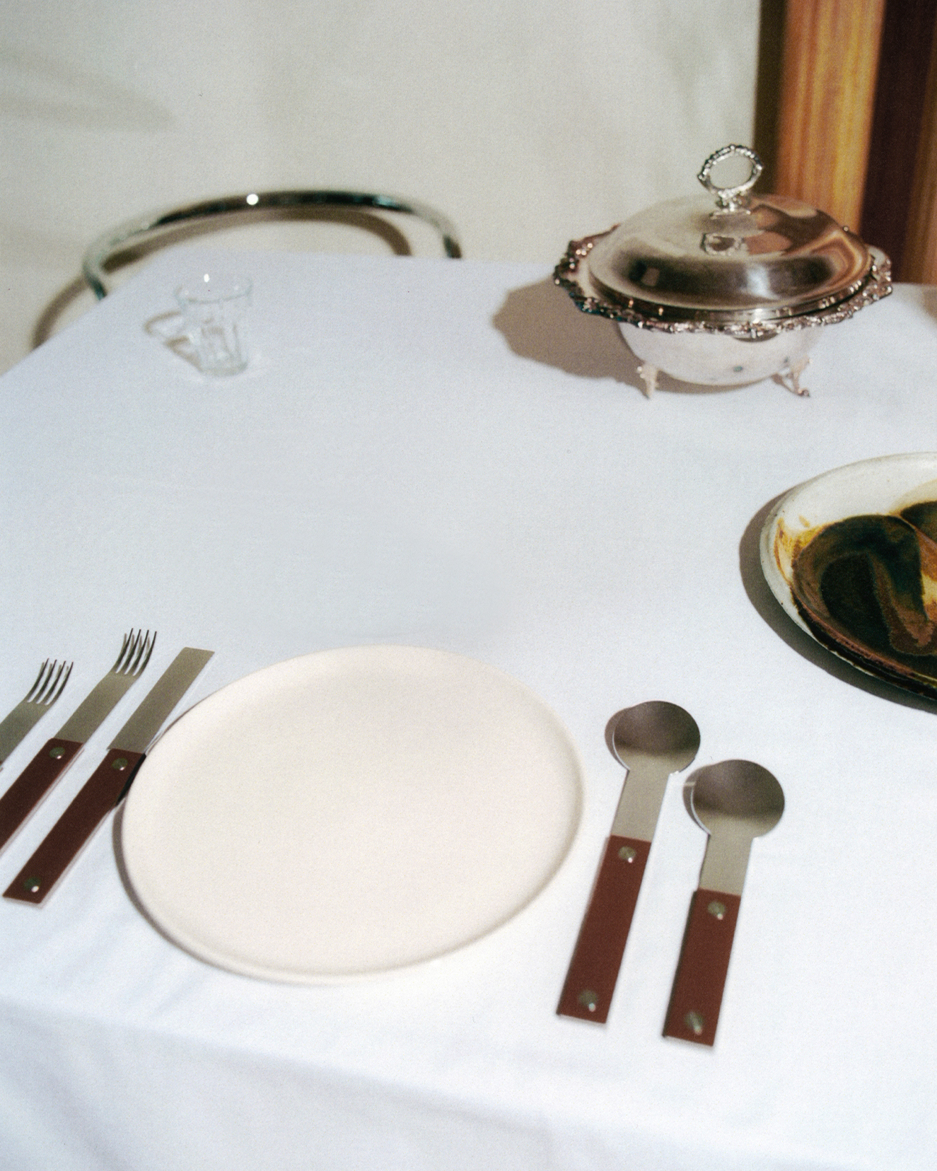 forks-plus-brown-flatware-place-setting-white-plate 5-piece brown-handled flatware place setting with white plate on white tablecloth, silver tray in background