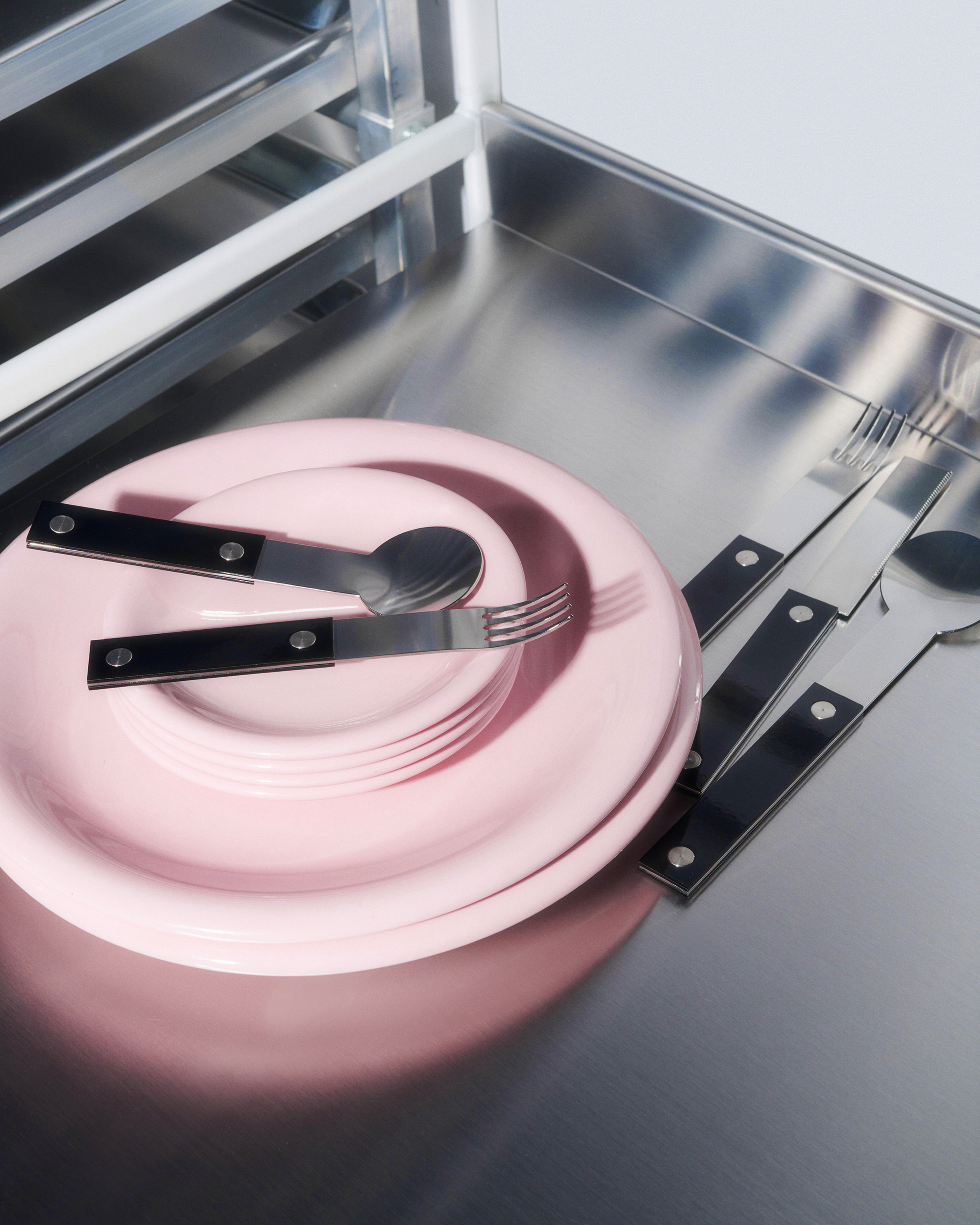Stainless steel flatware with black handles laying atop pink plates on a stainless steel surface.