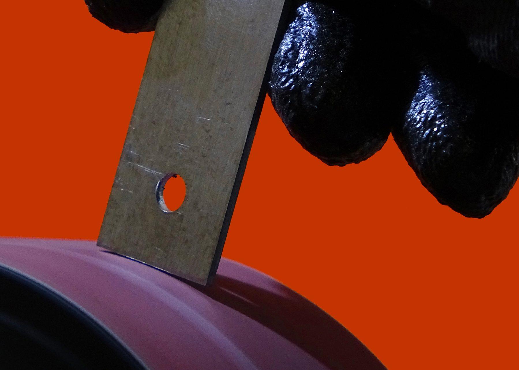 Black glove holding an unfinished handle belt sanding edge against a red backdrop.